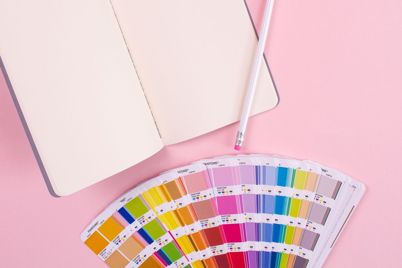 A photograph of a blank open notebook with paint colour swatches below on a pink background